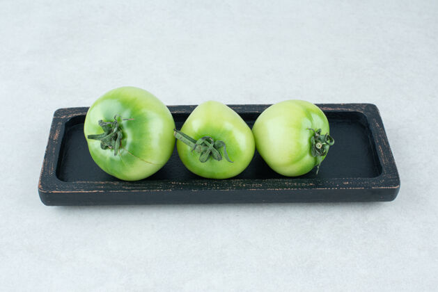 绿色腌青番茄放在黑盘子里新鲜蔬菜泡菜