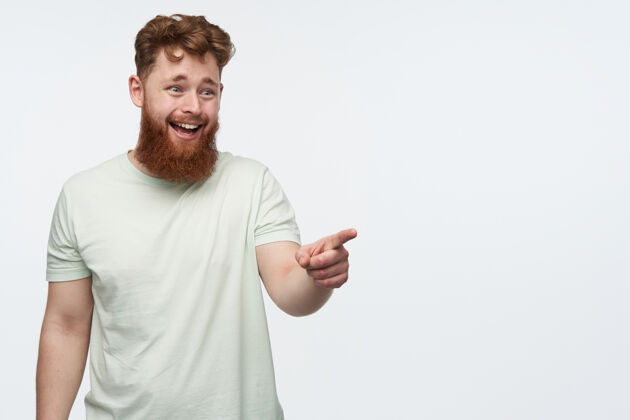 男人一个留着大胡子和红头发的年轻人的肖像 感到高兴和微笑 同时用手指在白色的右侧复印空间时尚红发生姜