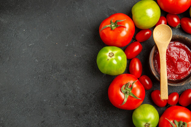 碗顶视图樱桃红色和绿色的西红柿围绕着一个碗 里面放着番茄酱和一个木勺 放在深色的桌子上 还有复印空间番茄酱苹果吃苹果