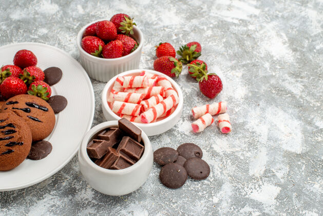 巧克力底视图饼干草莓和圆形巧克力在白色椭圆形盘子碗糖果草莓巧克力在灰白色桌子的左侧甜点壁板椭圆形