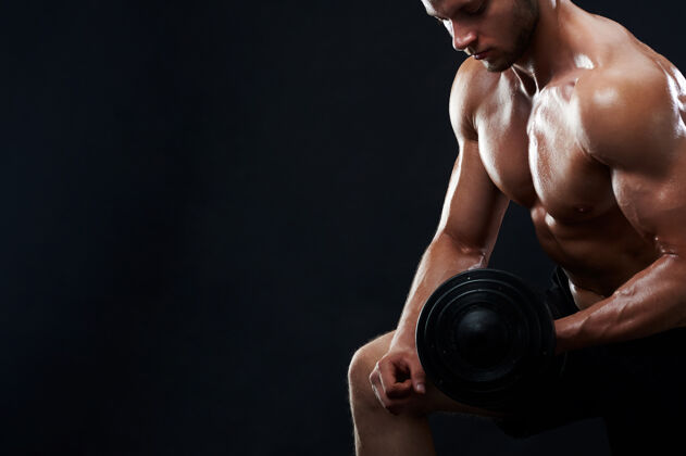 肌肉肌肉发达的年轻人在黑色背景下举重腹肌锻炼健身