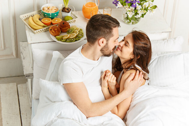 微笑年轻的异性恋夫妇躺在卧室的床上人女性枕头
