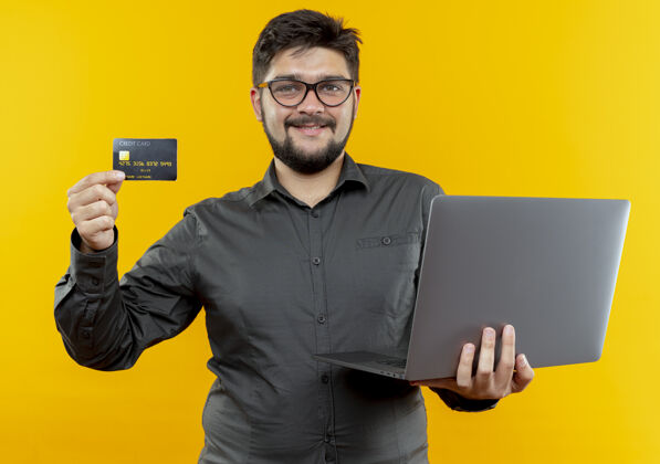年轻面带微笑的年轻商人戴着眼镜拿着笔记本电脑和信用卡持有笔记本电脑微笑