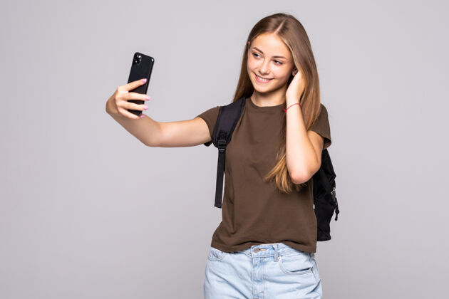 手机漂亮的年轻女子在白墙上的手机摄像头上自拍女性白色微笑