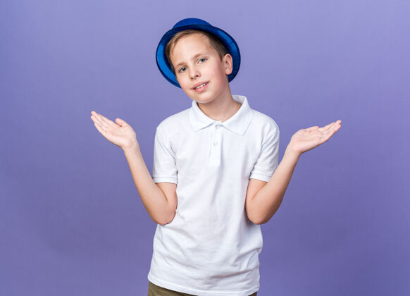 帽子高兴的年轻斯拉夫男孩与蓝色党帽子保持双手开放孤立的紫色墙上与复制空间孩子请保持年轻
