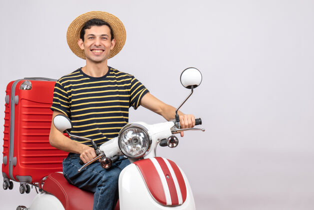 男性骑着轻便摩托车 提着红色手提箱的快乐年轻人的正视图手提箱快乐的年轻人景观