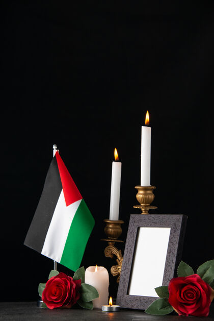 燃烧在黑暗的表面上点燃带着巴勒斯坦国旗和鲜花的蜡烛葬礼旗火