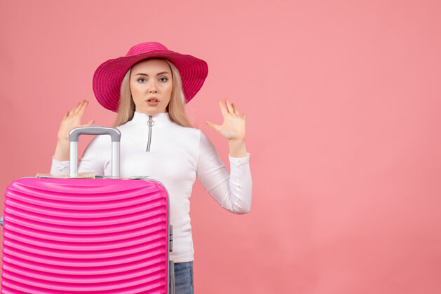 手正面图：躲在粉色手提箱后面的年轻女士举手帽子快乐快乐