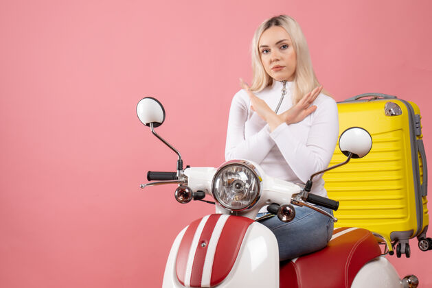 坐着前视图年轻的金发女郎骑着轻便摩托车双手交叉手摩托车前面