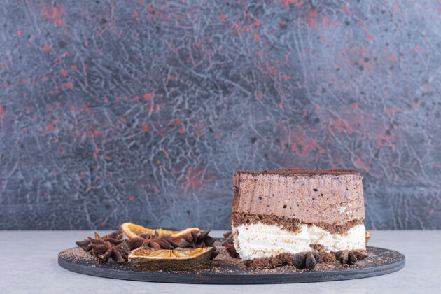 甜点一片巧克力蛋糕 加丁香和橘子片放在深色盘子里蛋糕巧克力小块