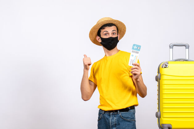 男人正面图：戴草帽的年轻人站在黄色手提箱旁 拿着旅行票 指着后面指着帽子黄色