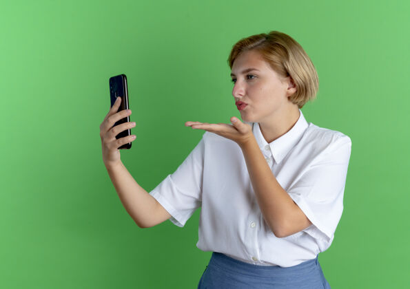 绿色年轻自信的俄罗斯金发女孩握着电话 用手送吻俄罗斯女孩发送