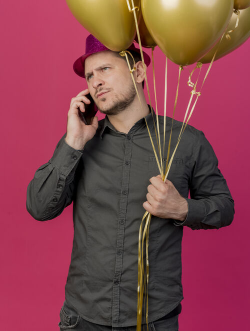 聚会严格的年轻人戴着粉红色的帽子拿着气球 在电话上说孤立的粉红色粉色穿壁板