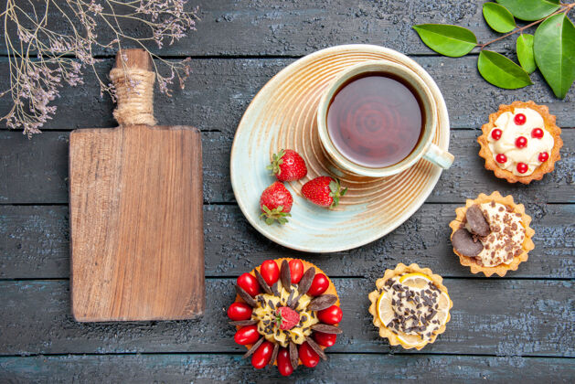 食物顶视图一杯茶和草莓放在茶碟上干橙子馅饼叶子浆果蛋糕和砧板放在深色的木桌上蛋糕碗茶