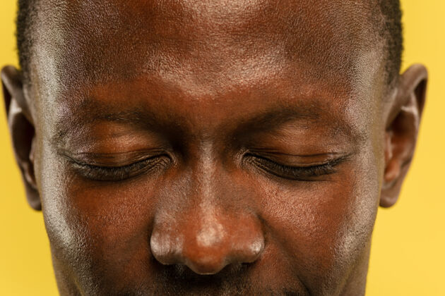 面部黄色摄影棚背景上的非洲裔美国年轻人的特写肖像皮肤保养良好的漂亮男模人类情感的概念 面部表情 销售 广告眼睛和脸颊年轻衬衫成人