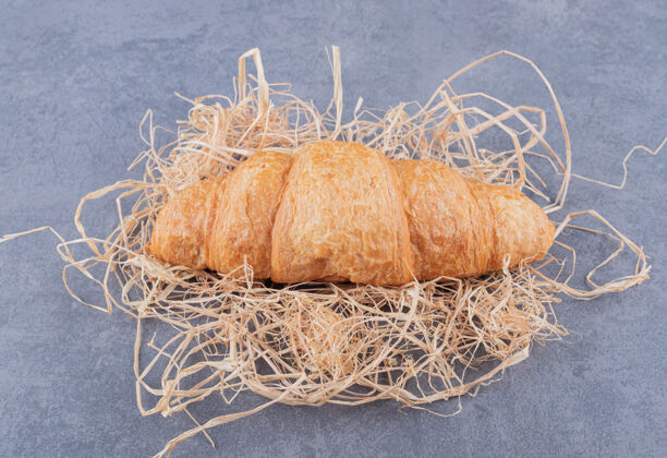 早晨新鲜的法国羊角面包在稻草上的特写照片 背景是灰色的法国面粉美食