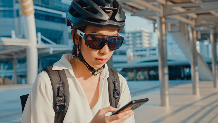 侧线亚洲女商人背着背包在城市街道上用手机上班自行车移动公司