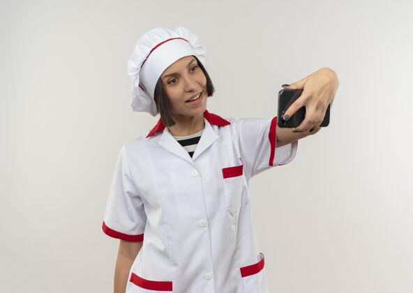 微笑微笑的年轻女厨师身着厨师制服 独自在白墙上自拍厨师感情年轻