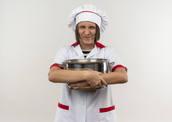 请高兴的年轻女厨师穿着厨师制服拿着锅看前面隔离的白墙上女脸人