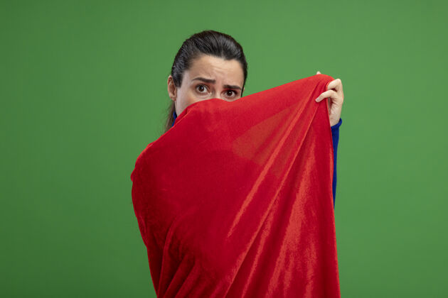 年轻年轻的超级英雄女孩惊讶地用斗篷遮住脸 隔离在绿色上掩护绿色脸