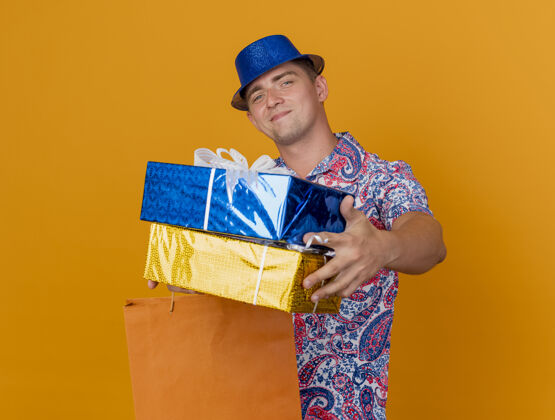 橙色高兴的年轻人戴着蓝色的帽子 拿着礼品盒和橙色的袋子隔离戴着派对小伙子