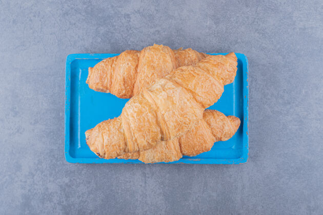 传统蓝色木板上三个新鲜牛角面包的顶视图桌布盘子餐厅