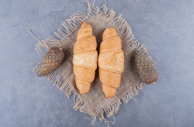 美味两个新鲜的羊角面包 灰色背景上装饰着松果烹饪美味许多