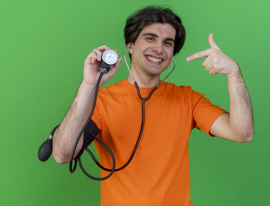 年轻带着听诊器的年轻人微笑着拿着血压计指着绿色的隔离带绿色听诊器点