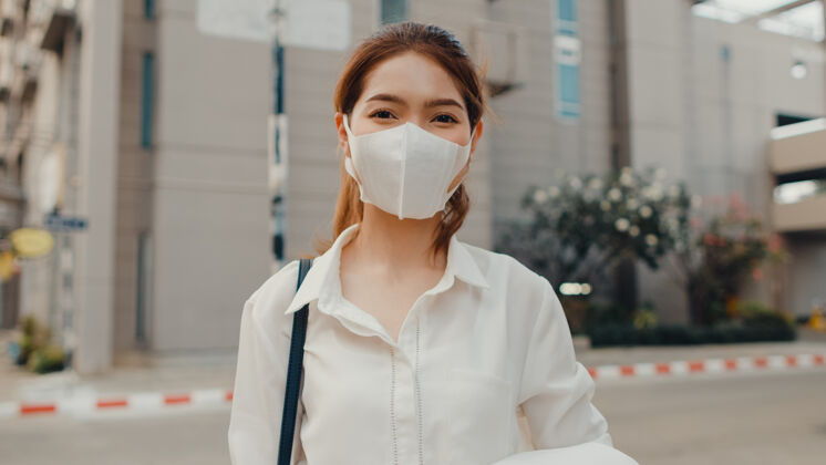 面具成功的亚洲年轻女商人穿着时尚的办公服 戴着医用面罩 在街上微笑着城市流行病医药