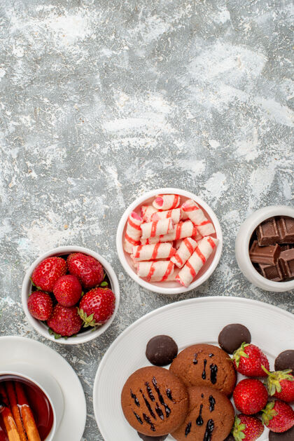 桌子上半部分查看饼干草莓和圆形巧克力在椭圆形盘子圆形的糖果草莓巧克力肉桂茶在灰白色的桌子底部碗盘子椭圆形茶