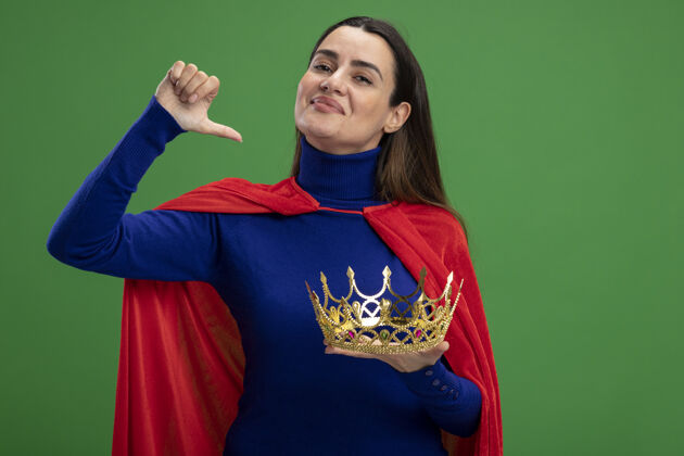 年轻高兴的年轻超级英雄女孩举着皇冠显示拇指下孤立的绿色显示绿色请