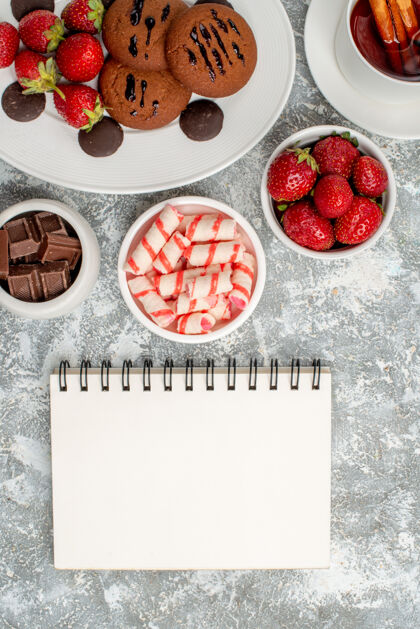 碗顶近距离观察饼干草莓和圆形巧克力放在椭圆形的盘子里一碗糖果草莓巧克力肉桂茶和一本笔记本放在灰白色的桌子上巧克力糖果甜点