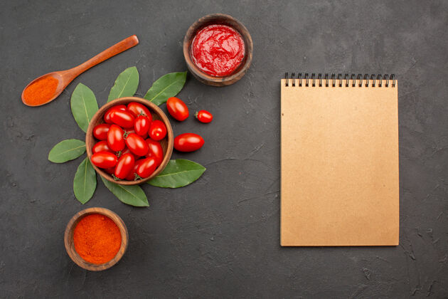 食物顶视图一碗樱桃西红柿 在黑桌子上放一个木勺 几碗番茄酱和辣椒粉 还有一本笔记本黑色桌子碗