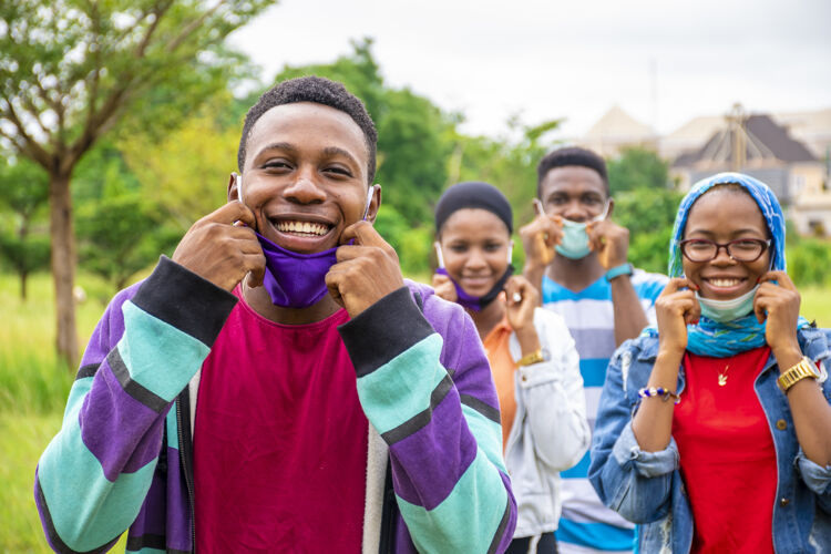 距离一群年轻快乐的非洲朋友戴着面具在公园里社交男性脸欢呼