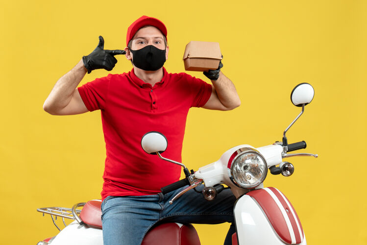 送货员俯视图微笑的送货员身穿红色上衣 戴着帽子手套 戴着医用面罩 坐在滑板车上 显示秩序衬衫手套摩托车