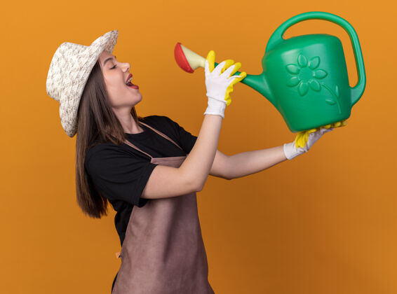 园艺漂亮的白人女园丁戴着园艺帽 戴着手套 假装喝橘子汁罐里的水浇水女请