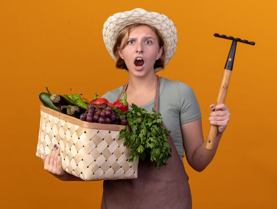 年轻焦急的年轻斯拉夫女园丁戴着园艺帽 手里拿着菜篮子 耙着桔子篮子蔬菜女性