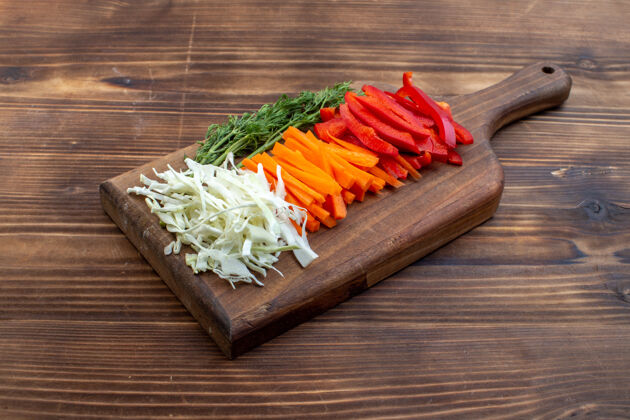 食物前视图切菜卷心菜胡萝卜青菜和胡椒切菜板棕色表面蔬菜沙拉盘子