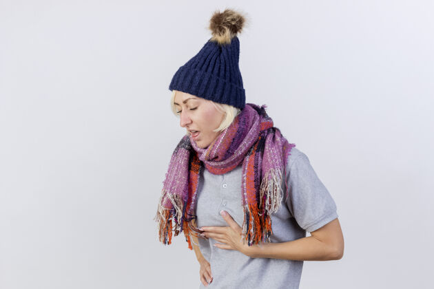 斯拉夫疼痛的年轻金发病斯拉夫妇女戴冬季帽子和围巾把手放在胸前隔离在白色墙壁与复制空间女人疼痛帽子