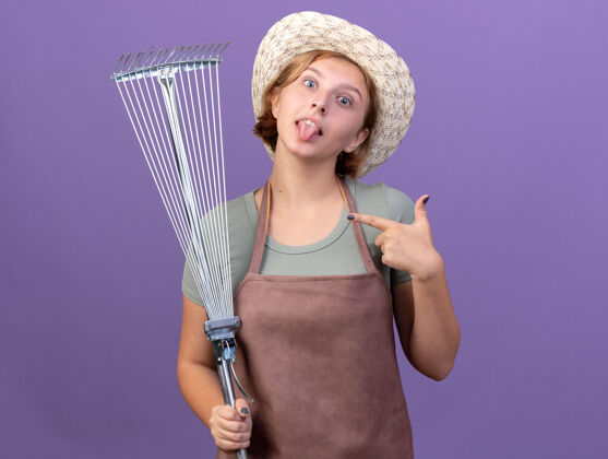 舌头给人印象深刻的年轻斯拉夫女园丁戴着园艺帽跺着舌头指着紫色的叶子耙帽子女性年轻