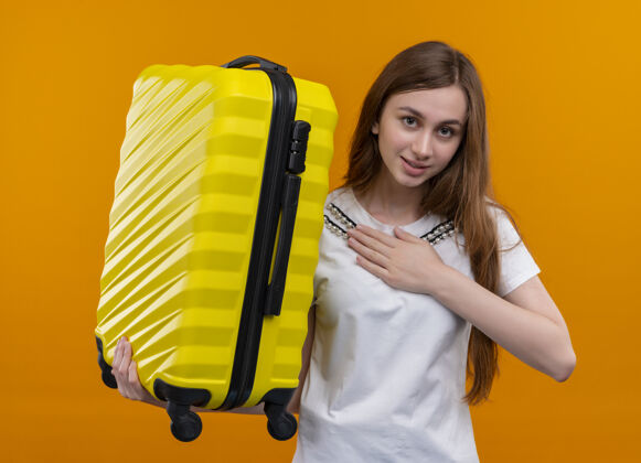 旅客在孤立的橙色空间里 年轻的旅行女孩拿着手提箱 把手放在胸前 很高兴手提箱女孩手