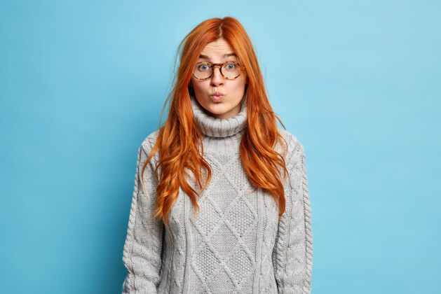 表情面部表情概念漂亮的红发欧洲女人保持嘴唇合拢 穿着针织毛衣看起来出人意料模特眼镜面部