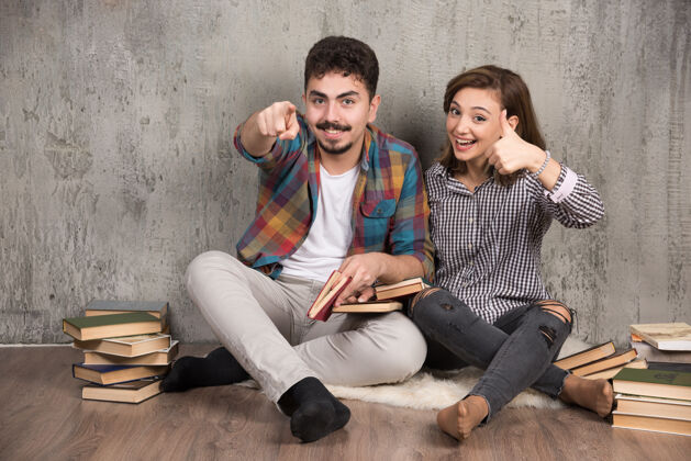 模特一对年轻夫妇拿着书坐在地板上 指着前面坐着情侣地板