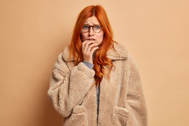 模特不高兴担心的红发女人咬指甲看起来很焦虑穿着暖和的皮衣棕色恐惧年轻