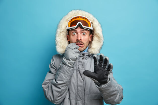 活动害怕情绪化的男滑雪者穿着暖和的夹克 戴着滑雪镜和手套 目不转睛地盯着已经活跃的寒假在山上度假年轻人害怕