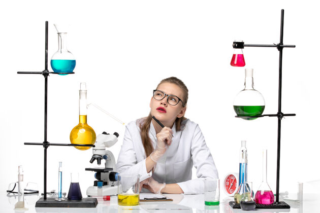 正面正面图身着医疗套装的女化学家在白色背景上写笔记和思考化学大流行健康病毒烧杯实验室容器