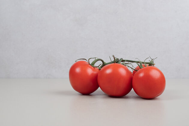许多在白色的桌子上放着一堆新鲜的红番茄和绿茎素食簇樱桃