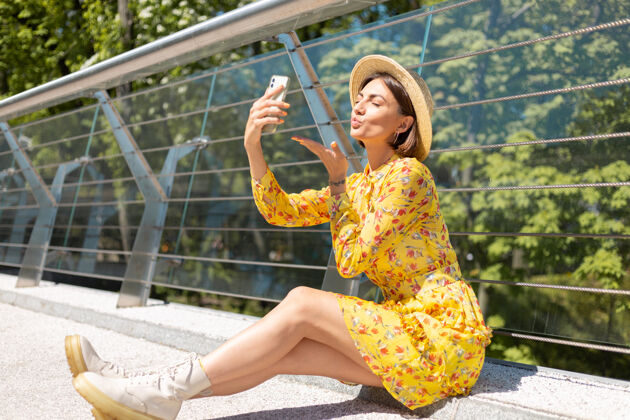 成功穿着黄色夏装的女人坐在桥上用手机自拍的户外写真街道城市户外