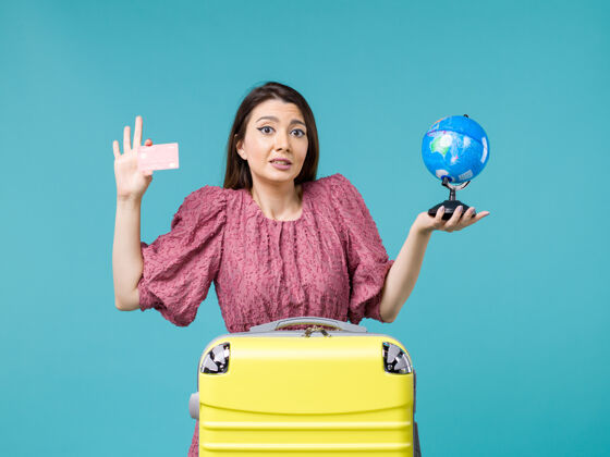 银行前视女性在旅途中手持小地球仪和红色银行卡在蓝色背景上航行旅程度假女性出海旅行红色航行小