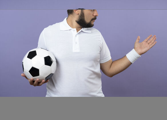持有年轻的运动型男子戴着头带和腕带 一边看一边拿着球 一边伸出手来足球男人壁板